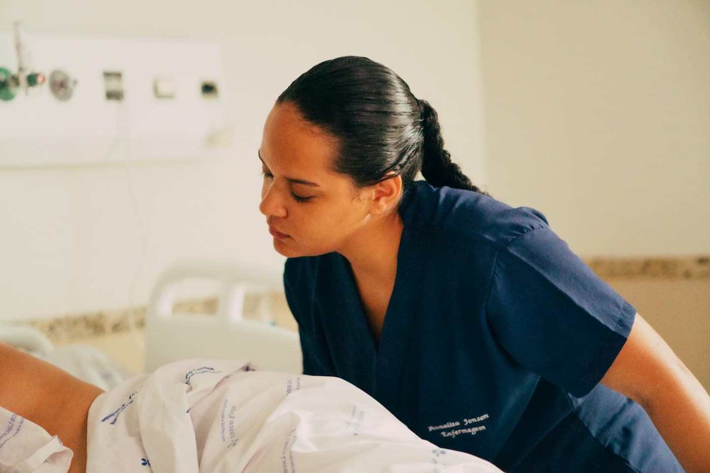 A nurse in navy scrubs leaning over to check on a patient in a hospital bed